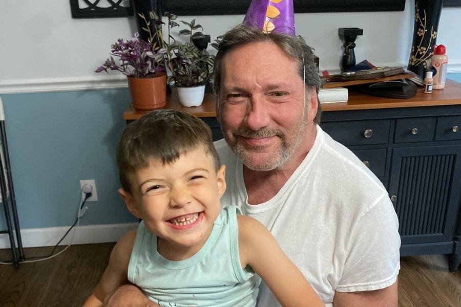 Alan Beck, retired NYPD officer, smiling and holding his young grandson Oriax in Rocky Point.